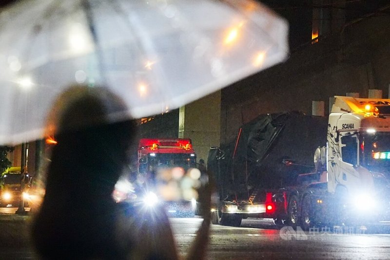 第2批M1A2T戰車27日晚間運抵台北港,裝載的卡車於28日凌晨離開港區大門。圖為民眾撐起雨傘在路口捕捉歷史性一刻。中央社記者游凱翔攝 114年7月28日