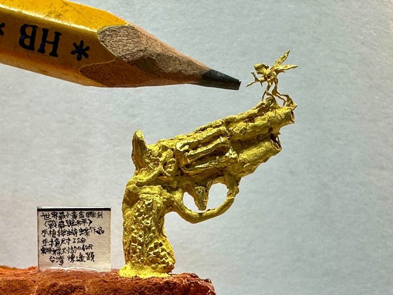 毫芒雕刻家陳逢顯8日發表新作「戰爭與和平」,槍口上站立1隻蝴蝶,象徵世界和平。黃金槍枝長度約2公分,蝴蝶平均尺寸僅0.4公分,在鉛筆尖前顯得渺小。(陳逢顯提供)中央社記者黃旭昇新北傳真 114年8月8日