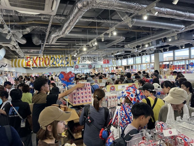 大阪世博自4月13日開幕至本月20日,進場遊客突破1500萬人。暑假遊客大增,平均一天13萬4000人。圖為8月19日會場西門附近商店遊客多景象。中央社記者楊明珠大阪攝 114年8月21日