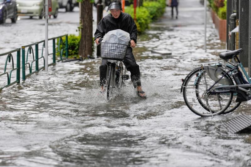 東京民眾11日騎腳踏車涉水。(美聯社)