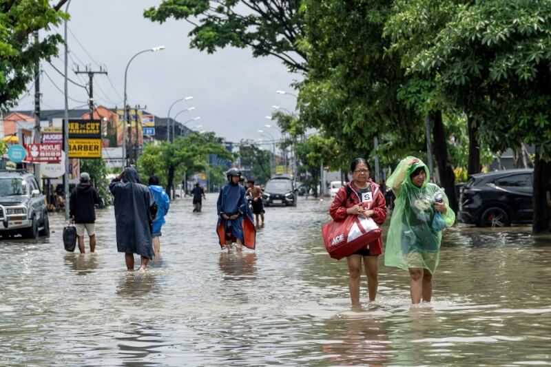 居民拿著行李走過被洪水淹沒的街道。(路透社)
