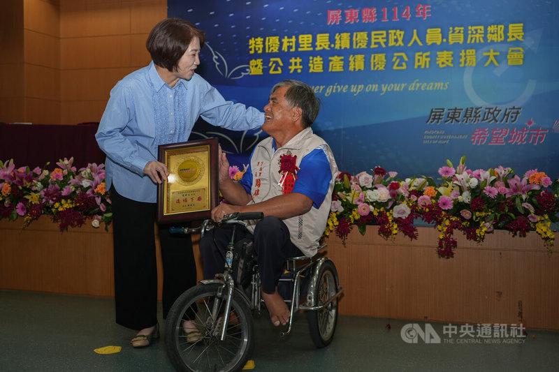 屏東縣政府12日表揚年度特優村里長，東港鎮下廍里長周錦谷（右）雖為身障人士，仍騎特製行動車服務里民，立下身障不設限榜樣，縣長周春米（左）頒發獎牌。中央社記者黃郁菁攝　114年9月12日