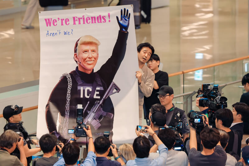 一名男子在入境大廳持上頭畫著川普作美國移民暨海關執法局裝束的大型海報。(韓聯社)