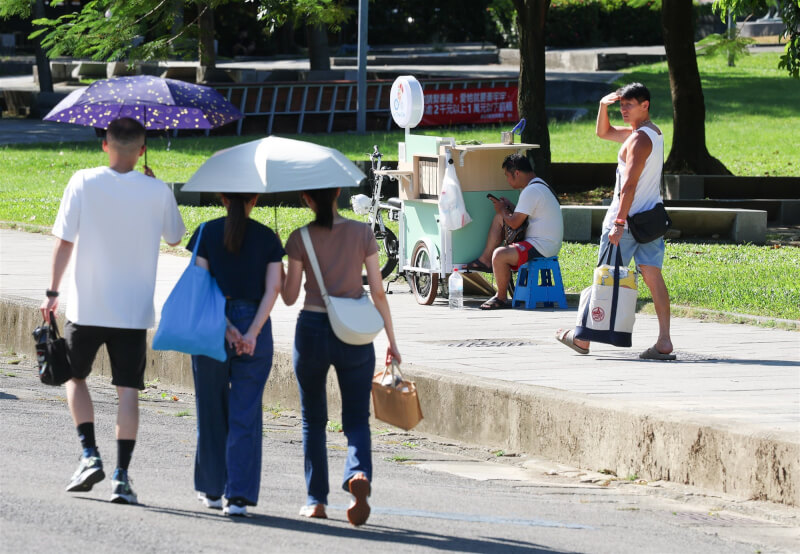 圖為台北華山大草原周邊午後民眾或撐傘、或以手遮擋烈陽,攤車業者也在陰影處躲太陽。(中央社檔案照片)