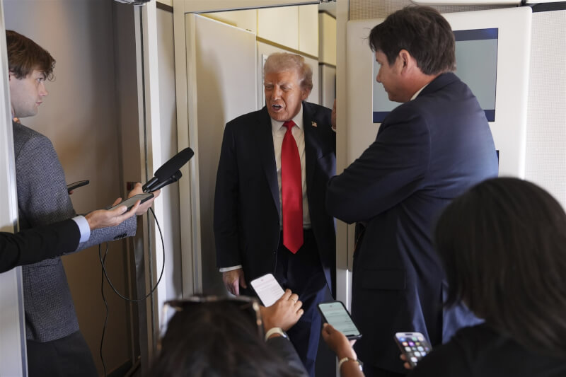 美國總統川普（中）在飛往倫敦的空軍一號上與記者交談。（美聯社）