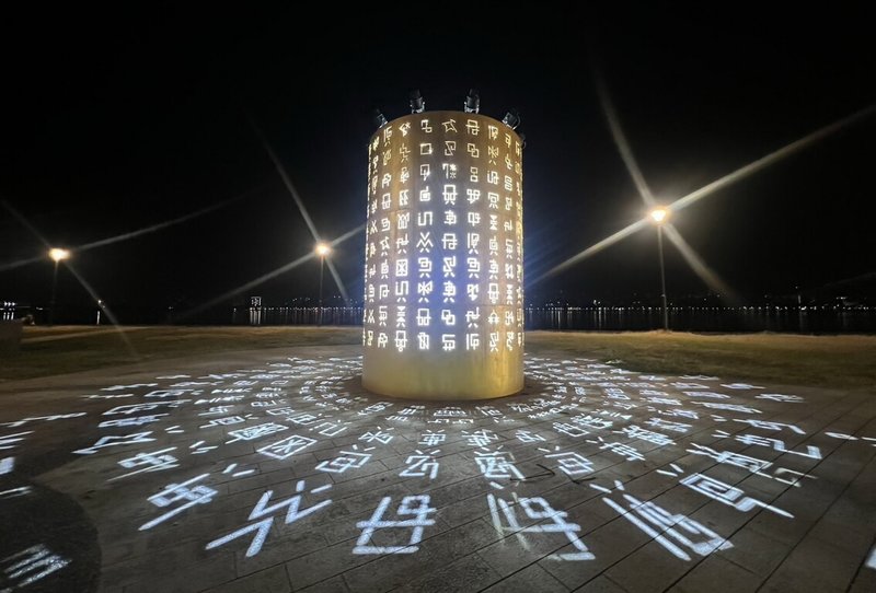 2025八里城市沙雕展與經典日系動漫「數碼寶貝」聯名,以「被選召的孩子們」為主題,設計4大章節共22座沙雕及6座光雕,其中光雕藝術裝置「八大徽章之光」為刻滿數碼文字的圓柱形作品。(新北市高灘地管理處提供)中央社記者黃旭昇新北市傳真 114年9月20日