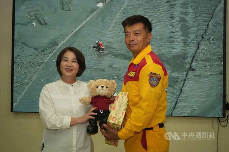 屏東縣特搜大隊支援花蓮災區階段性任務結束,26日返抵屏東,縣長周春米(左)特別前往特搜大隊基地致贈加菜金與紀念品,由大隊長陳世鴻(右)代表接下消防小熊。中央社記者黃郁菁攝 114年9月26日