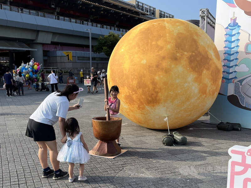 中秋連假首日，民眾帶著小朋友到台北圓山花博公園參與2025商圈嘉年華，在巨型月亮造型氣球布景前體驗搗麻糬。中央社記者徐肇昌攝　114年10月4日