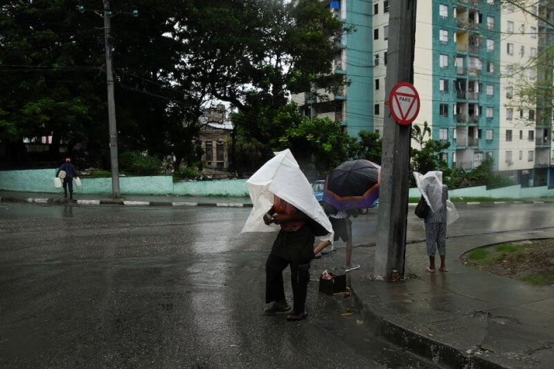 颶風美莉莎重創古巴第二大城聖地牙哥,一名男子28日用塑膠布遮雨過馬路。(路透社)