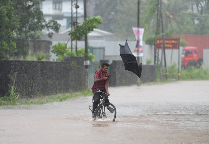 氣旋迪特瓦在斯里蘭卡帶來豪雨及洪患，一名男子28日騎自行車行經積水的街道時，雨傘被強風吹壞。（路透社）