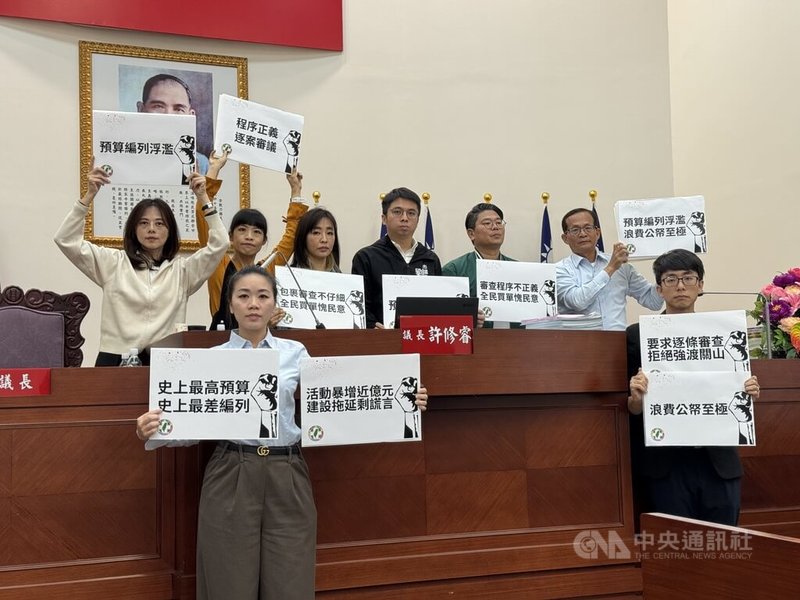 新竹市議會2日進行「審議提案」，民進黨團9名市議員各自拿著標語霸占主席台，高舉「預算編列浮濫、浪費公帑至極」與「要求逐條審查」等標語。中央社記者魯鋼駿攝　114年12月2日