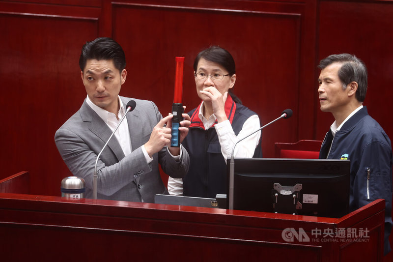 民進黨台北市議員洪婉臻2日質詢時把北市警局所使用的酒測棒交給市長蔣萬安（左），並指出明明是「中國貨」卻被洗產地貼牌賣入警局，要求啟動調查。蔣萬安表示，相關器材皆依警政署共約採購，會檢討並向中央反映。右為台北市警察局長李西河。中央社記者王騰毅攝  114年12月2日