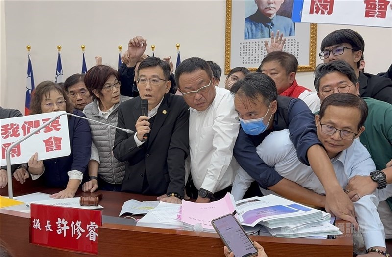 民進黨籍新竹市議員2日上午手持標語占據市議會主席台杯葛議事，下午國民黨、新聯線政團議員以人數優勢搶回後，議長許修睿（前左3）才總算宣布開議，議場內場面一度是相當混亂。 中央社記者魯鋼駿攝　114年12月2日