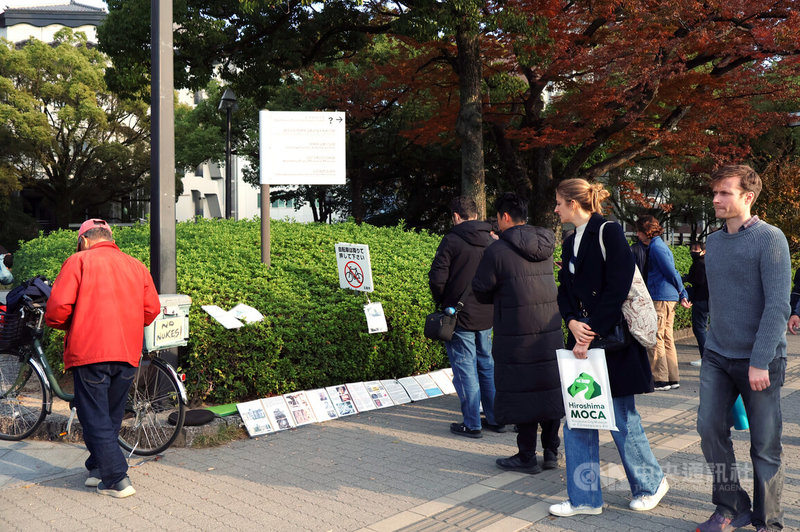 在原爆圓頂旁，原是英文老師的三登浩成（身著紅衣者），近18年來每天都在廣島原爆頂旁講述原爆歷史，不少遊客駐足細讀放置在地板的英文文宣，攝於11月21日。中央社記者謝怡璇廣島攝　114年12月5日