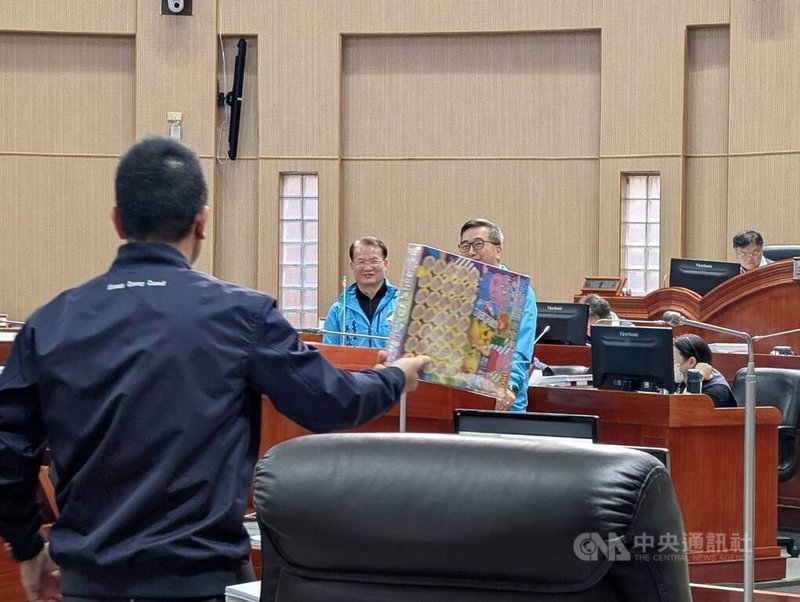 無黨籍金門縣議員董森堡（背對者）10日質詢時送抽抽樂玩具給金酒公司，董森堡表示，希望金酒提高產品價值，而非酒品市面庫存沒有做精準計算，酒品銷售不出去就讓抽籤讓民眾買酒，應努力開拓國內外市場。中央社記者吳玟嶸攝　114年12月10日