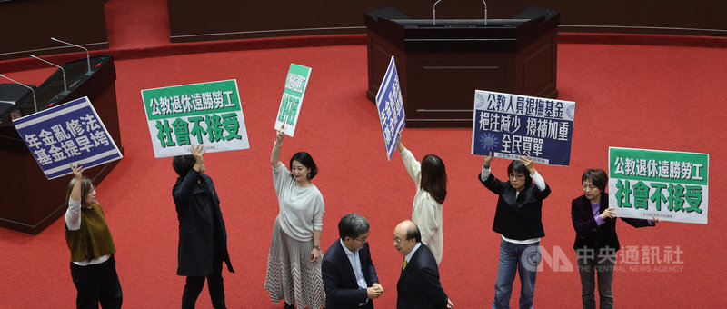 立法院會12日經表決，三讀修正通過公務人員退休資遣撫卹法部分條文。表決時，朝野立委也在議場內攻防，民進黨立委們高舉標語表達立場。中央社記者趙世勳攝　114年12月12日
