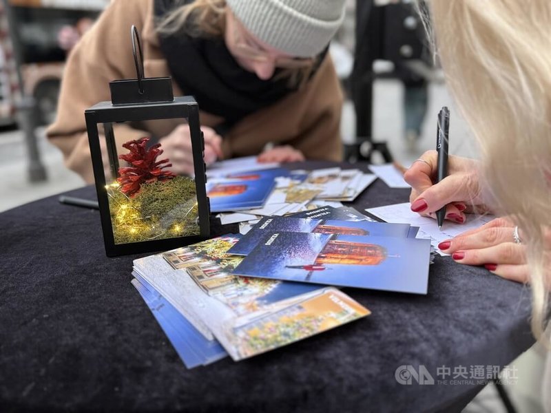立陶宛首都維爾紐斯舉辦「耶誕節前的耶誕節」活動,官方旅遊推廣單位Go Vilnius在市區多個地點放置耶誕明信片與郵筒,免費供民眾寄送至海外,向親友傳遞節日祝福。桌上的紅色松果為「耶誕貨幣」。中央社記者游堯茹維爾紐斯攝 114年12月14日