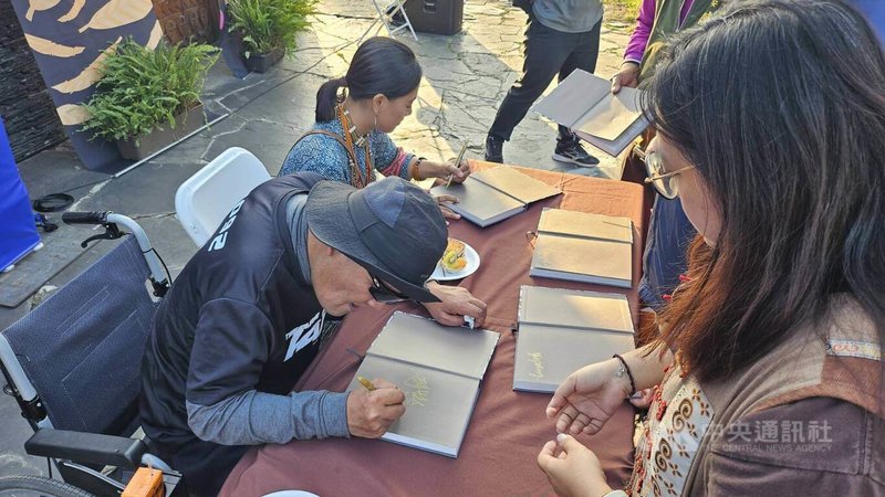 排灣族藝術家秦榮輝（阿瀨）（前左）跨足文學領域，與攝影師張之萓（後左）合著詩集「部落的風」，16日在屏東泰武國小石板屋前正式發表，現場也舉辦簽書會。中央社記者黃郁菁傳真　114年12月16日