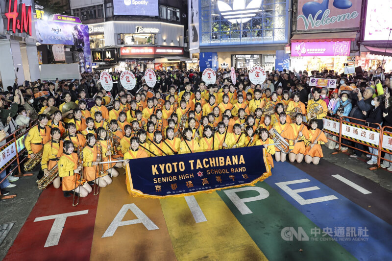 日本京都橘高校吹奏樂部18日再度應邀來台，晚間到訪台北西門徒步區快閃演出，有「橘色惡魔」之稱的團員們穿上橘黃色亮麗制服，在知名地標彩虹地景上留影。中央社記者鄭清元攝　114年12月18日
