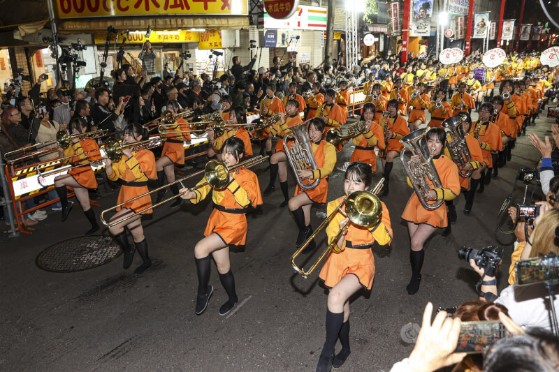 有「橘色惡魔」之稱的日本京都橘高校吹奏樂部18日再度跨海來台,晚間快閃台北西門徒步區為民眾送上大型行進管樂演出,整齊隊形與悠揚樂聲吸引人潮爭睹。中央社記者鄭清元攝 114年12月18日