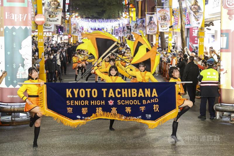 被暱稱為「橘色惡魔」的日本京都橘高校吹奏樂部18日晚間快閃現身台北西門町徒步區,踏著整齊隊形帶來精彩踩街演出,吸引大批人潮共賞,感受熱情活力。中央社記者鄭清元攝 114年12月18日