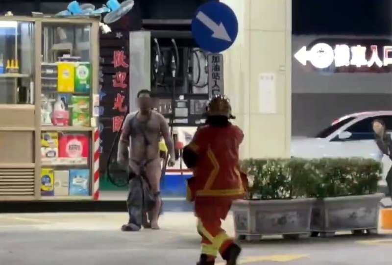 新北市板橋區民族路加油站9日晚間發生民眾點火,引發火警並波及正在加油的保全員事件。警方10日表示,犯嫌一度追打消防隊員,消防員已提出傷害與妨害公務罪告訴;圖為犯嫌遊走,與戒護的消防員對峙。(徐姓民眾提供)中央社記者黃旭昇新北傳真 115年1月10日