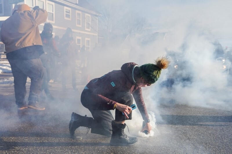 圖為美國明尼蘇達州13日的一場移民掃蕩行動，一名男子拿東西覆蓋住警方發射的催淚瓦斯。（路透社）