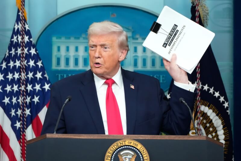 美國總統川普20日執政滿週年，他在記者會上展示一大疊寫滿執政週年成就的文件。（美聯社）