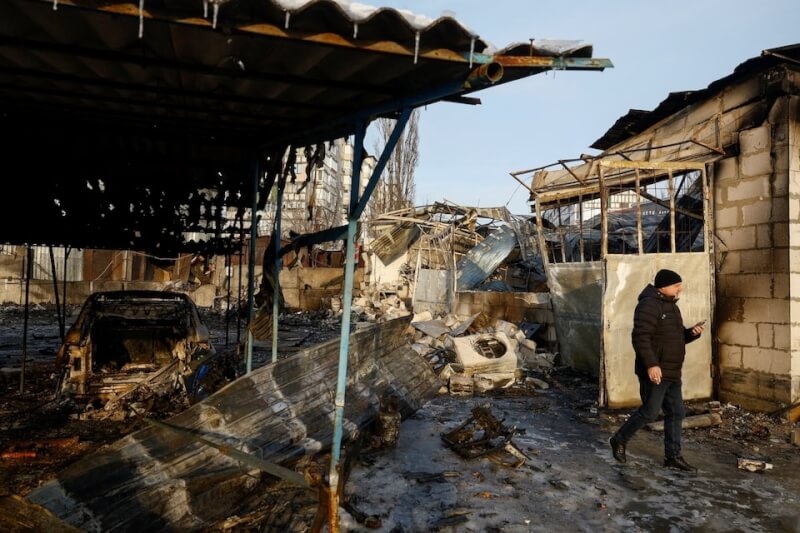 俄軍24日向烏克蘭發動襲擊，基輔居民行經一處毀損的汽車修理廠。（路透社）