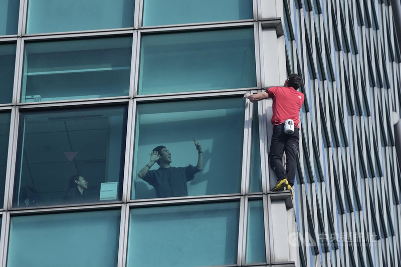 美國自由攀岩好手霍諾德徒手攀登台北101大樓，一名民眾在大樓玻璃窗內開心拍攝。中央社記者徐肇昌攝 115年1月25日