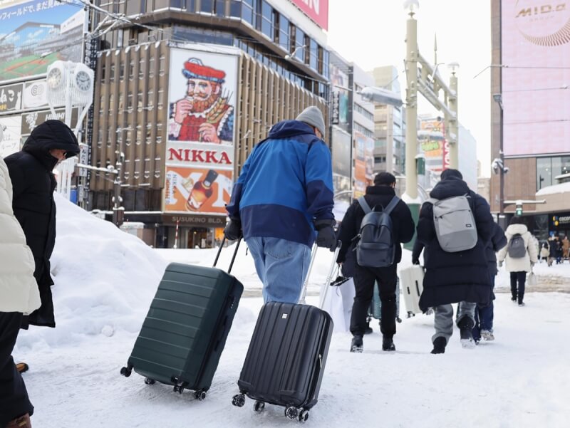 日本北海道大雪，札幌市區民眾26日拖著行李箱在積雪的道路行走。（共同社）