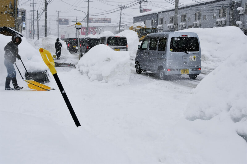 青森縣2日持續降雪，路旁除雪民眾推起的積雪高過車頂。（共同社）