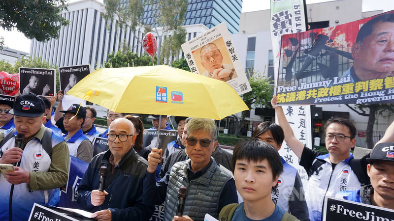抗議人士聚集在洛杉磯中國領事館前，手舉蘋果日報發送的黃色雨傘，聲援黎智英。前排右1為流亡海外的香港青年梁啟駿。中央社記者林宏翰洛杉磯攝　115年2月15日