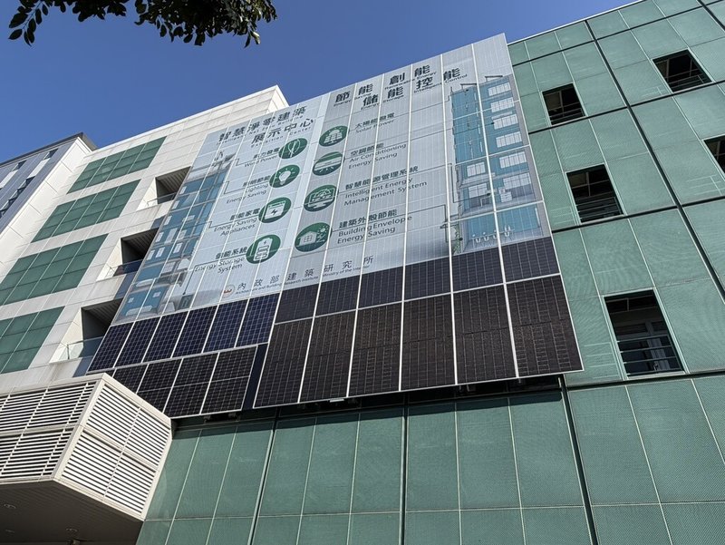 睿田能源公司與內政部建築研究所合作，在台北市萬隆捷運站附近的建研所智慧化居住空間展示中心大樓外牆，外掛彩繪立面太陽光電板，以白底綠圖呈現智慧淨零建築成果。其左半部採噴印式固定彩繪技術、右半部為可撕換式彩繪技術，下方未彩繪的太陽能板為刻意呈現的對比。（民眾提供）中央社記者高華謙傳真　115年2月20日