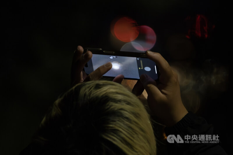 圖為去年9月8日午夜凌晨，民眾在文化大學後山拿起手機抓拍月全食身影。（中央社檔案照片）
