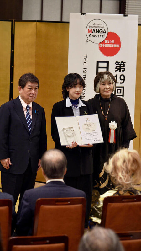 日本外務省主辦的第19屆日本國際漫畫獎頒獎典禮4日在東京飯倉公館舉行。台灣漫畫家南南日（中）以作品「Mararum：山間料理人」榮獲優秀獎（銀獎），手持獎狀與日本外務大臣茂木敏充（左）、評審長里中滿智子（右）合影。（台灣文化中心提供）中央社記者戴雅真東京傳真　115年3月4日