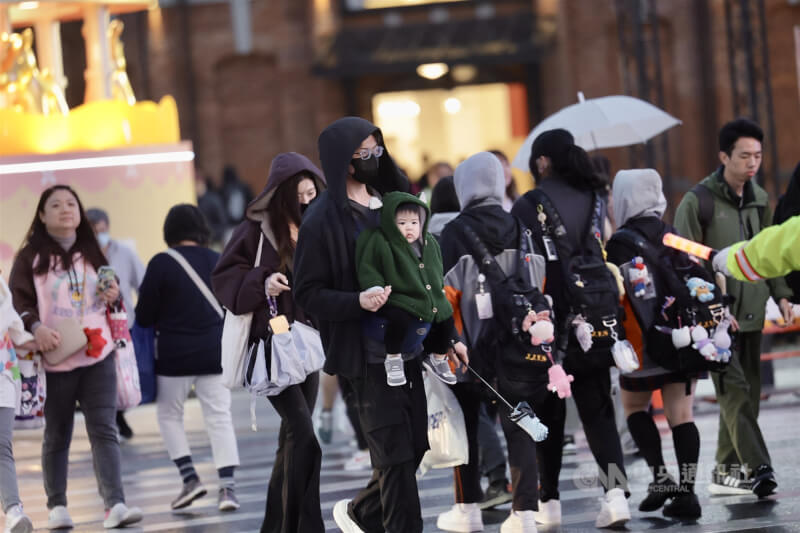 中央氣象署表示，9日及12日將接連有冷氣團南下。圖為台北西門商圈街頭家長為孩子戴起帽子保暖、遮擋細雨。（中央社檔案照片）