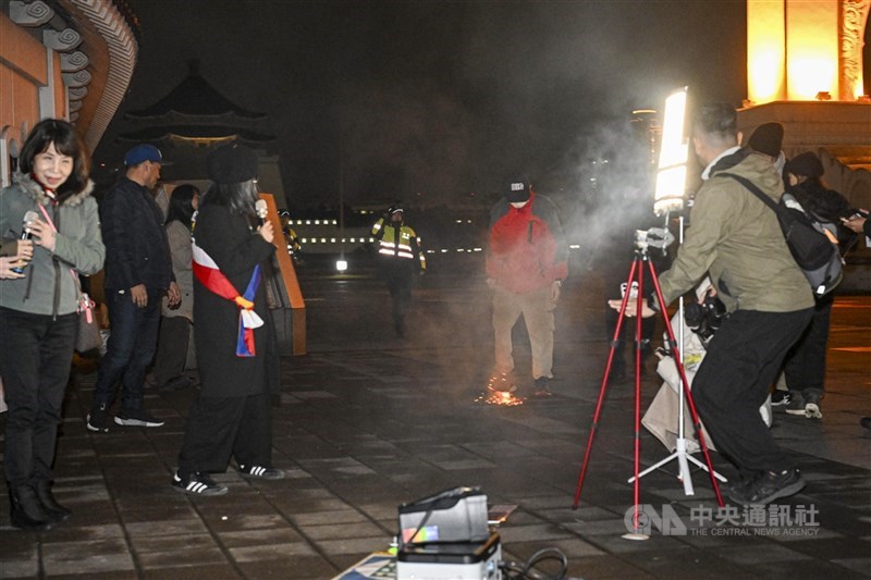 在台藏人團體10日晚間在台北自由廣場舉行西藏抗暴67週年燭光晚會，現場一名男子（後右紅衣者）活動中突然扔擲鞭炮，地面一度爆出火花與煙霧。人權團體今天發出譴責聲明。（中央社檔案照片）