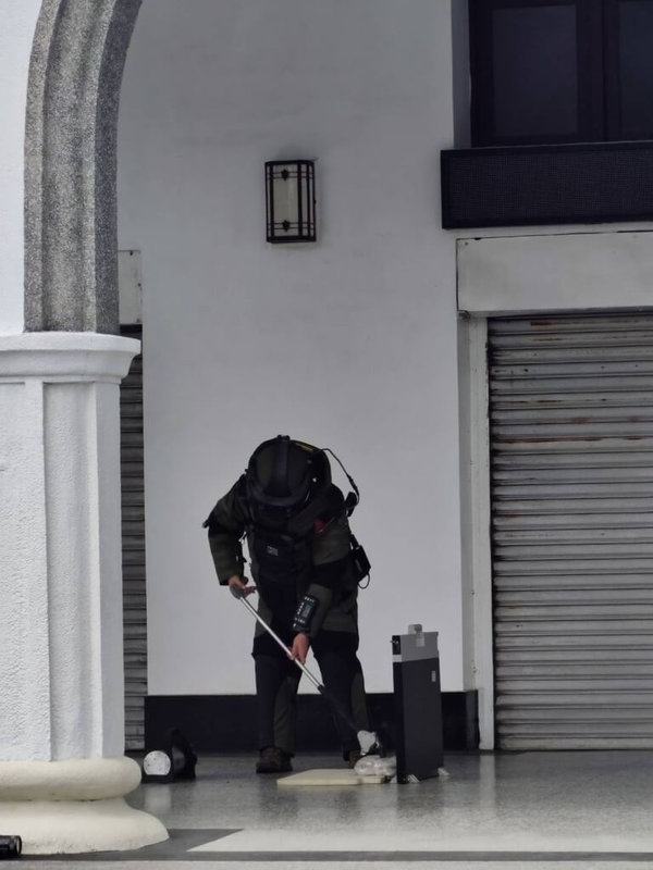 花蓮地方法院大門21日遭不明人士放置可疑包裹，防爆小組到場後拉起封鎖線，人員全副武裝謹慎處理，現場以X光機掃描檢視包裹，並將紙袋放入防爆箱內。（花蓮地檢署提供）中央社記者張祈傳真　115年3月21日
