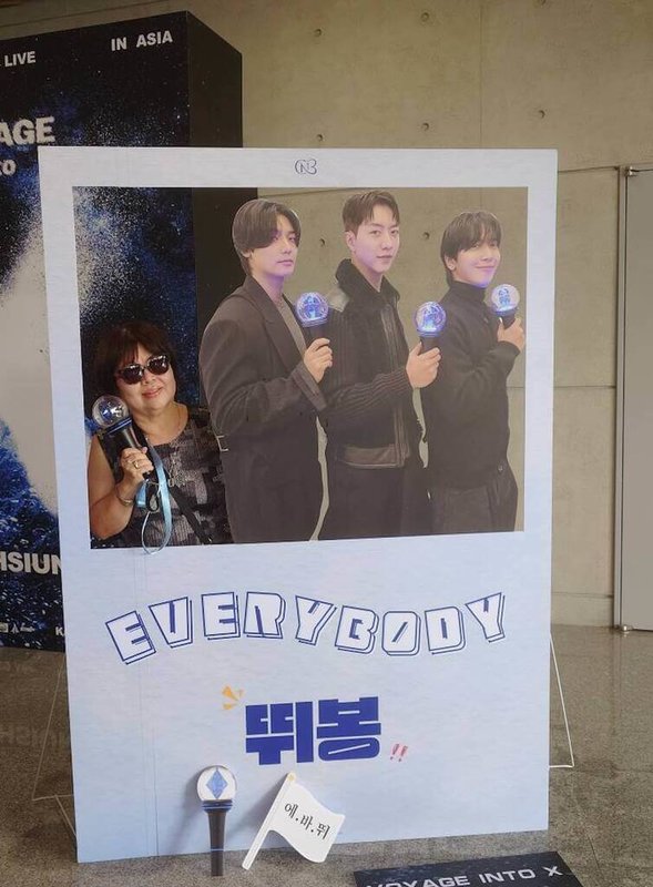 69歲退休護理師姚姐(化名)(圖),希望健康活到75歲,每個月看一場演唱會,圖為參加韓國樂團CNBLUE演唱會,在場外與活動立牌合影。(讀者提供) 中央社記者陳婕翎傳真 115年3月22日