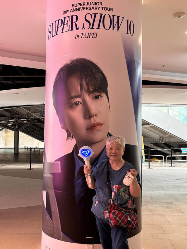 84歲的陳奶奶（圖）因為韓國綜藝節目「新西遊記」第一次認識到Super Junior成員圭賢，演唱會入場前，她開心地與圭賢的廣告柱合影。（讀者提供） 中央社記者陳婕翎傳真　115年3月22日