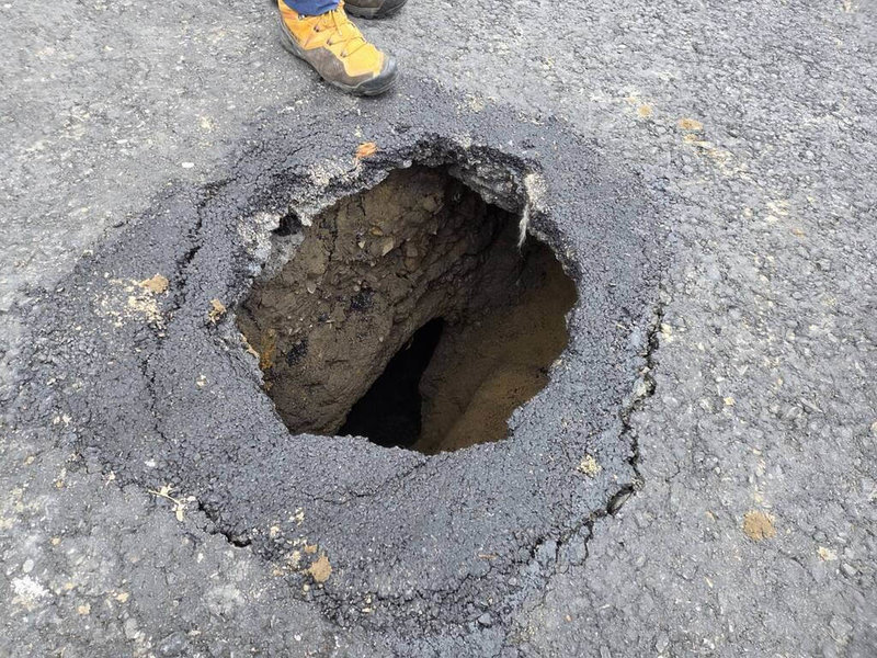 基隆市基金三路往大武崙方向路面25日突然出現坑洞，經勘查，確認為舊排水系統陰井側壁破損，將先以鐵皮等物品擋住破損側壁後，以「控制性低強度回填材料」（CLSM）灌入坑洞暫時修復，目標下午5時前完成。（讀者提供）中央社記者王朝鈺傳真　115年3月25日