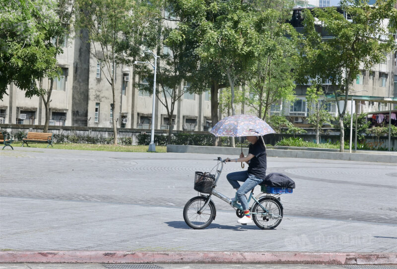 圖為台北市松山區民眾騎單車撐傘遮陽。（中央社檔案照片）