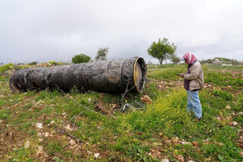 伊朗向以色列發射多枚飛彈，約旦河西岸的一名村民26日站在伊朗飛彈殘骸旁。（路透社）