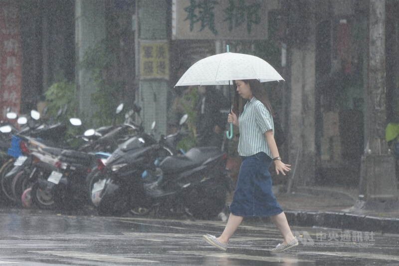 圖為民眾撐傘穿越台北市北投區的斑馬線。（中央社檔案照片）