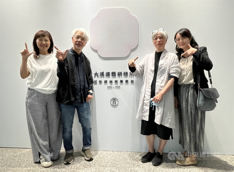 大溪漆藝研修所所長鳥毛清（左2）、理事長陳美霞（右2）、助教陳愷靜（右1），以及家樂福文教基金會執行長蘇筱駗於第2屆大溪漆藝研修班畢業展入口合影，並比出「7」的手勢，取其與「漆」同音之意。圖攝於115年4月5日。中央社記者黎桑尼攝　115年4月9日