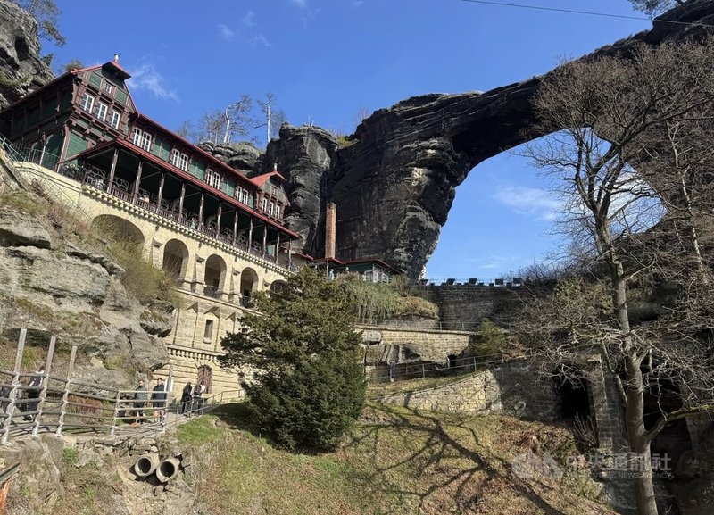 捷克的波希米亞瑞士國家公園（Bohemian Switzerland National Park）有峽谷、岩柱與天然拱門等景觀。這裡有歐洲最壯觀的天然拱岩之一，巨大的灰黑色拱岩橫亙在岩壁上，一旁是紅色與綠色的木造餐廳，形成鮮明對比。中央社記者劉郁葶波希米亞瑞士國家公園攝　115年4月12日