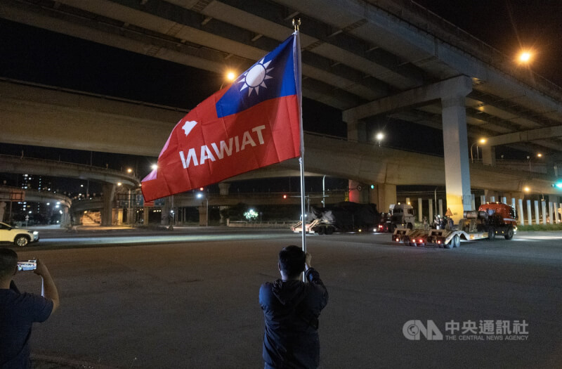 多輛民間拖板車27日駛出台北港，板車上乘載被黑色防水布包裹的M1A2T戰車，現場也有軍事愛好者帶著國旗為國軍加油打氣。中央社記者趙世勳攝　115年4月27日