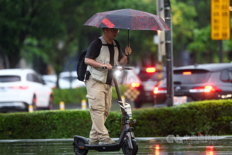 圖為桃園市中壢區街頭有民眾在陰雨天中邊騎滑板車邊撐傘。（中央社檔案照片）