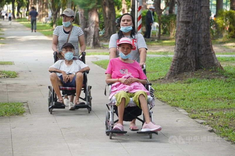 圖為家庭看護移工推著乘坐輪椅的長者在高雄市新興區一處公園內散步。（中央社檔案照片）